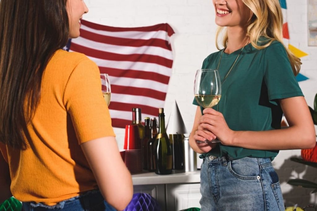 smiling young women drinking wine and talking at a 4th of july home party
