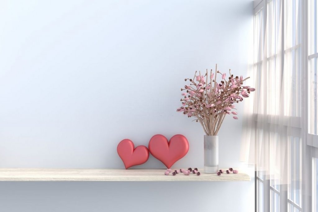 White living room decor with two hearts and pink flower vase on a wall mounted table