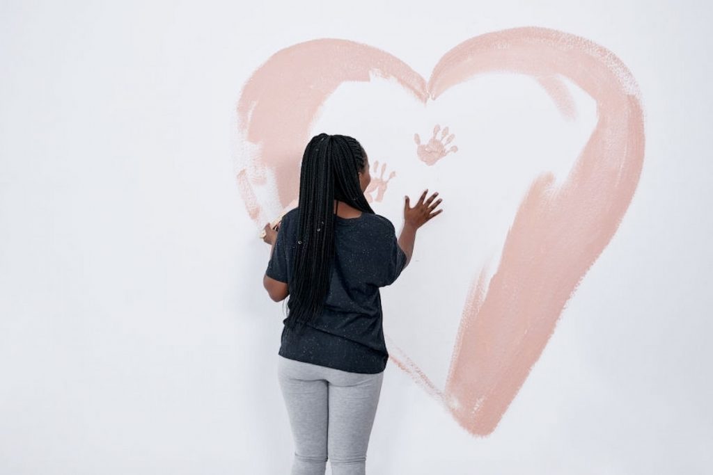 a girl is drawing on the white wall a heart shape with pink paint