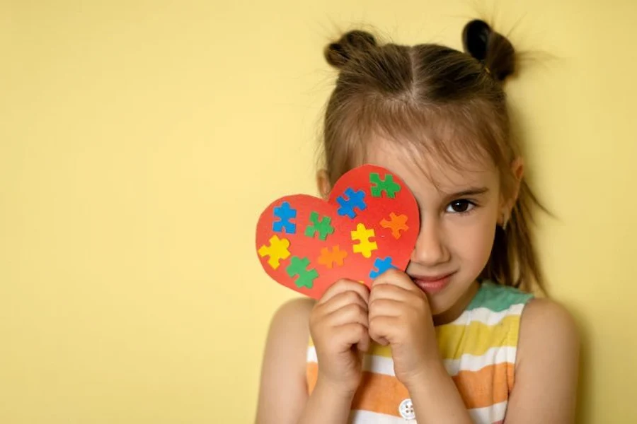 a little autistic girl holding a heart shaped piece of colorful puzzles