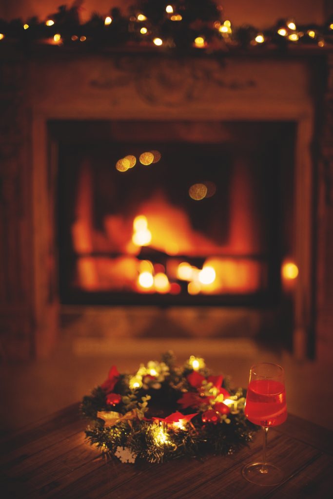 Christmas wreath, glass of champagne and blurred background burning fireplace with fire